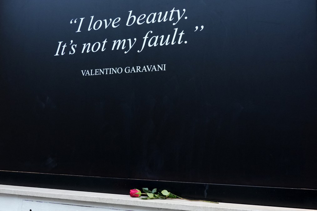 A red rose is laid by Valentino's shop window covered with a black poster reading "I love beauty, It is not my fault - Valentino Garavani",