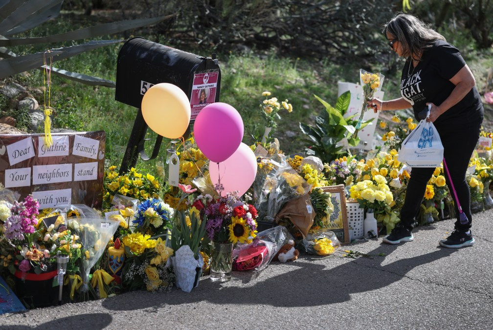 Karla C. places flowers in a memorial set up next to the driveway leading to Nancy Guthrie's residence