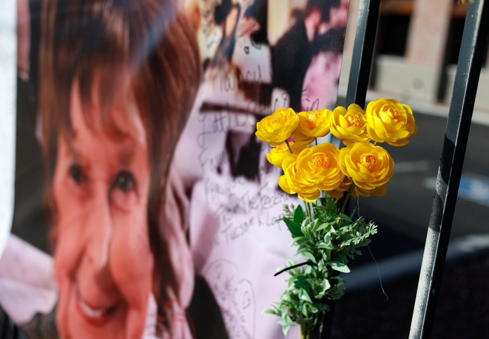 Yellow flowers hang from a photograph of Nancy Guthrie that is displayed on a banner
