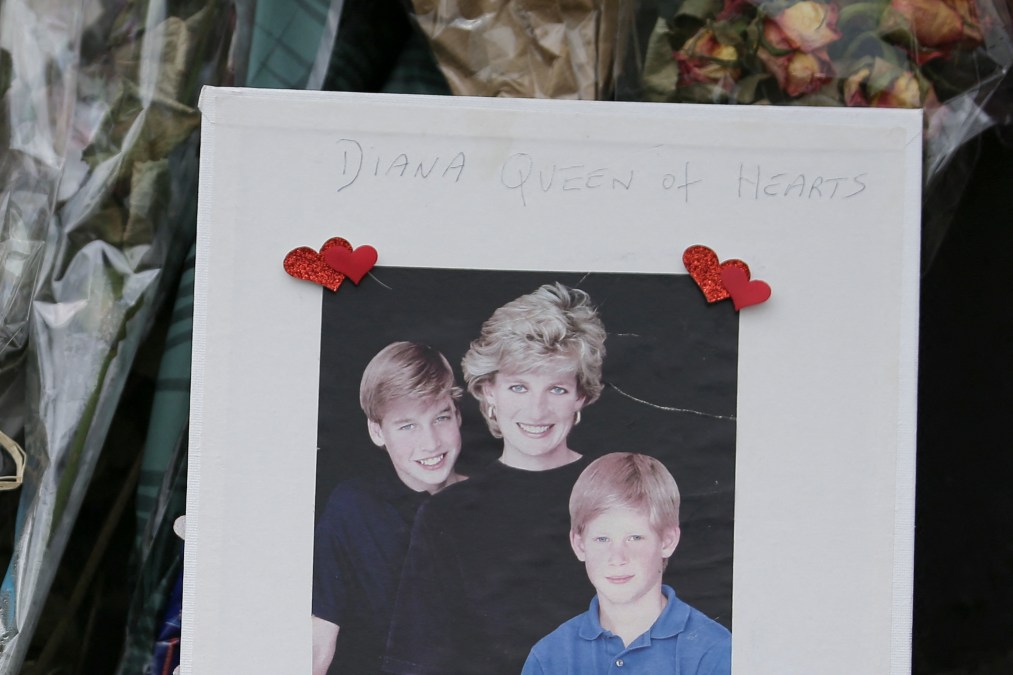 A photograph of Diana, Princess of Wales (C) with her sons Britain's Prince William, Duke of Cambridge, (L) and Britain's Prince Harry (R) is seen with floral tributes left outside Kensington Palace in Central London on August 29, 2017 ahead of the 20th anniversary of Princess Diana's death. 