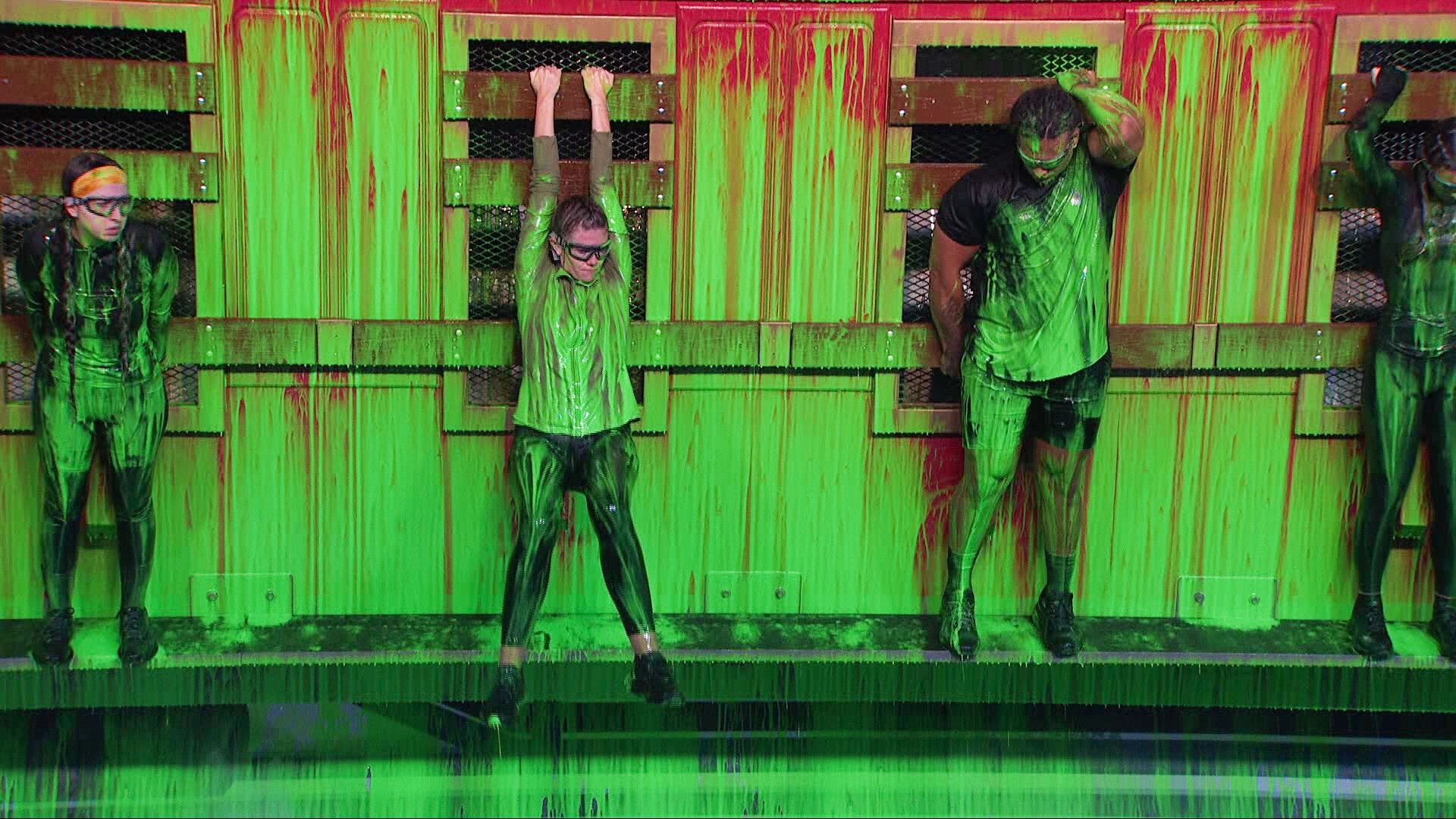 Ava Pearl, Kelley Morgensen and Keanu Soto hang onto a wall covered in green paint.