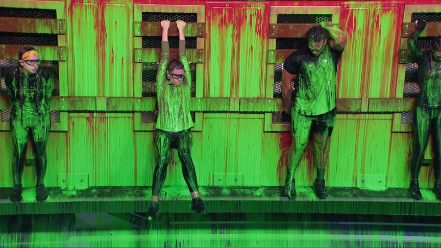 Ava Pearl, Kelley Morgensen and Keanu Soto hang onto a wall covered in green paint.