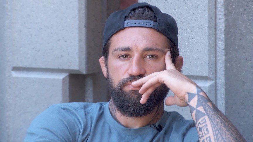 Kamu Kirk sits outside and rest his head on his hand.