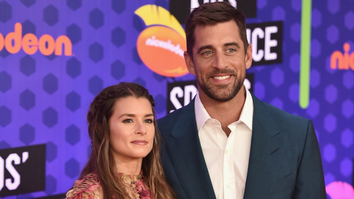 Aaron Rodgers smiles in a blue suit next to Danica Patrick.