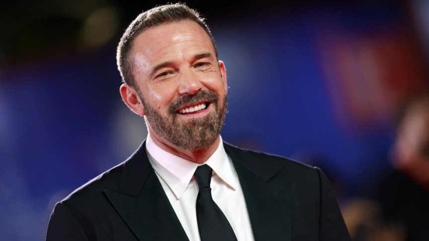 Ben Affleck smiles as he wears a black suit and tie.