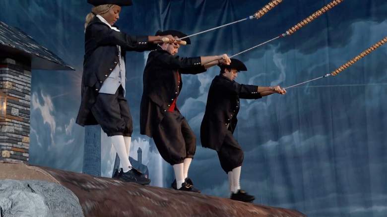 Taylor Brown, Rick Devens, and Drew Campbell are dressed as colonists as they stand on a platform.