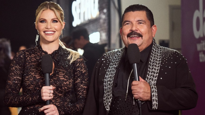 Witney Carson and Guillermo Rodiguez hold microphones in black dance costumes.