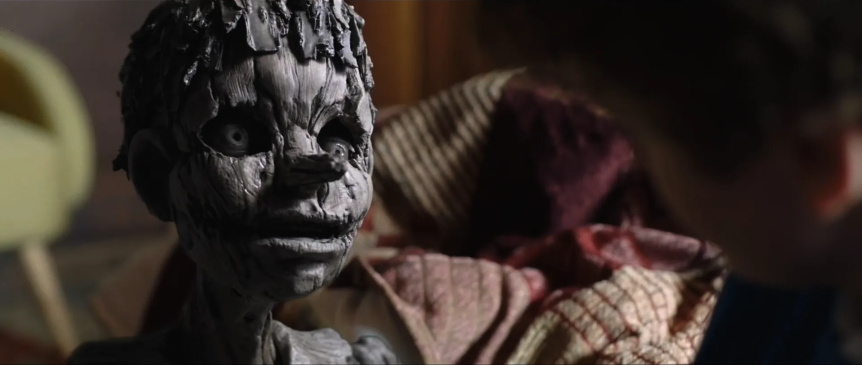 Close‑up of the Pinnochio practical effect; cracked grain, hollow eyes, and an eerie half‑open mouth, with a blurred background showing the use of lens and focus